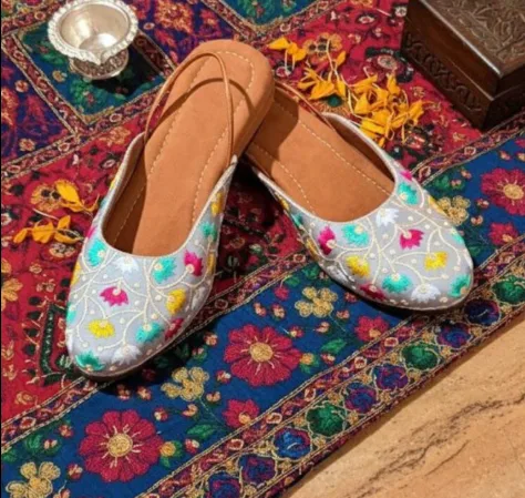 This is a pair of white Punjabi juttis featuring vibrant floral embroidery